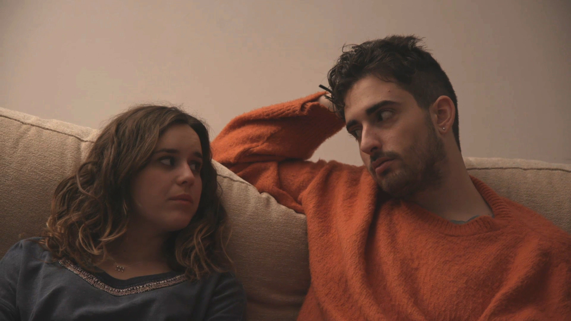 Una noia i un noi (Maria Sanz i Adrián Portillo) asseguts còmodament en un sofà. Hi ha poca llum i tots dos es miren d'una manera còmplice.
