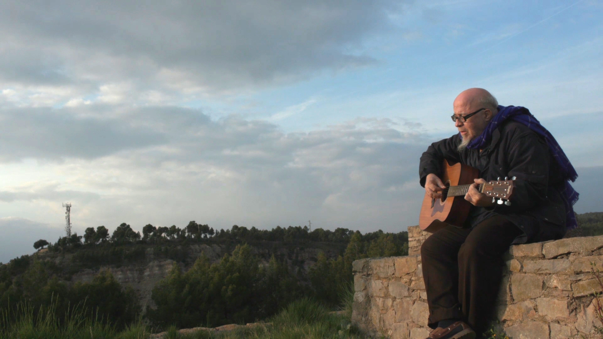 A les ruïnes d'un castell medieval, un home d'una setantena d'anys (Quico Palomar), amb poc cabell i una mica de barba, toca una cançó amb una guitarra. Al fons hi ha molts arbres i un cel amb núvols.